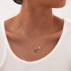 Detail of paperclip necklace with diamond safety pin and blue heart pendant on model