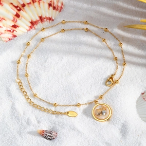Detailed close-up of golden shell pendant with K18 stamp on a sandy beach background