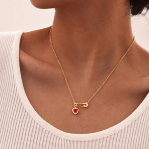 Detail of a gold-plated paperclip safety pin necklace with a red heart-shaped gemstone pendant