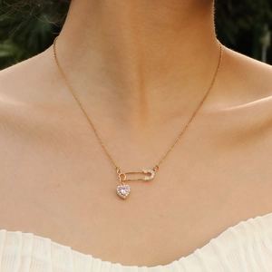 Detail of gold paperclip necklace with pink heart pendant worn on a model