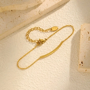 Bracelet en acier doré à perles et barre courbée sur fond de pierre minimaliste
