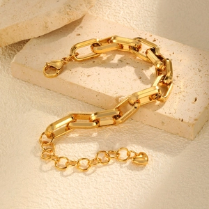 Close-up of golden chunky link bracelet with heart charm on a textured stone base