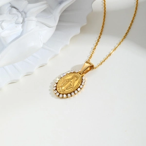 Gold oval Virgin Mary necklace with crystal frame on a classic white plaster background