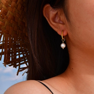 Détail de boucles d'oreilles vintage en or avec perle blanche portées par un mannequin en été