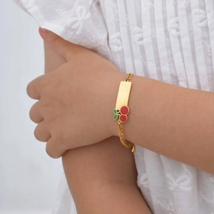 Bracelet enfant en acier doré avec plaque à graver et breloque cerise sur un modèle