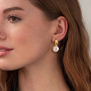 Gros plan d'un mannequin portant des boucles d'oreilles dorées en C avec une grosse perle