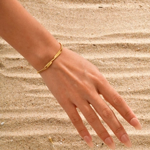 Bracelet Mobius doré avec plaque rectangulaire sur poignet féminin sur sable de plage