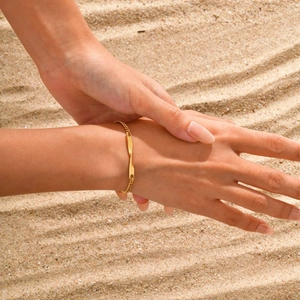 Détail d'un bracelet Mobius doré avec chaîne à gourmette sur la main contre le sable