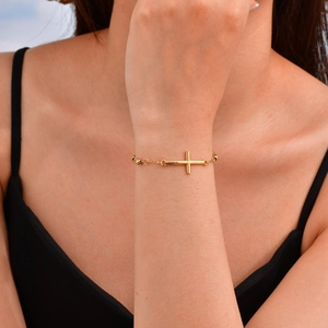 Primer plano de una pulsera de cuentas de acero inoxidable dorado con dije de cruz en la muñeca