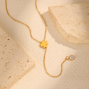 Detalle de collar en Y de trébol dorado con colgante de circón sobre fondo de piedra beige