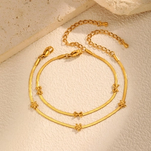 Bracelets chaîne serpent dorés avec breloques papillon et fleur sur pierre beige