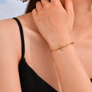 Primer plano detallado de una pulsera de cuentas doradas con cruz en la muñeca