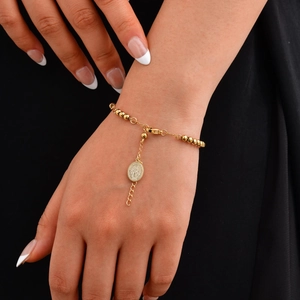 Detalle de pulsera de cuentas doradas con medalla de Virgen María y cruz en la muñeca