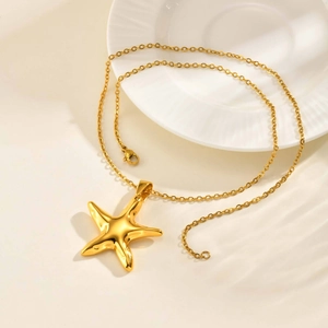 Vue détaillée d'un collier pendentif étoile de mer dorée sur surface blanche