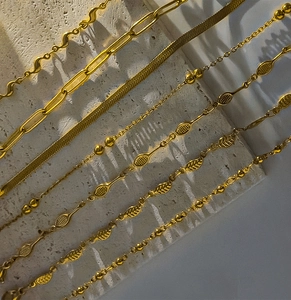 Detail view of seven different styles of gold stainless steel chains on stone texture