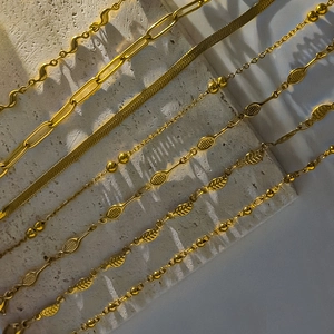 Golden stainless steel anklets featuring racket and leaf charms on natural stone surface
