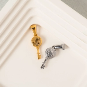 Polished gold and silver St. Benedict key pendants on a minimalist white display