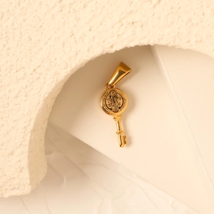 Detailed view of a gold Saint Benedict medal key pendant on an artistic stone background