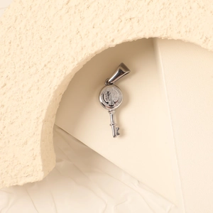 Macro detail of silver St. Benedict Medal key pendant on minimalist stone pedestal