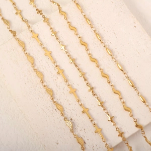 Colliers dorés en acier inoxydable avec feuille et croix sur une surface en pierre texturée