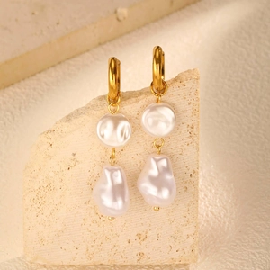 Detail of baroque pearl drop earrings hanging on a stone display with golden hoop hooks