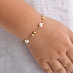 Close-up of girls gold chain bracelet with white pearls and polished bow charms