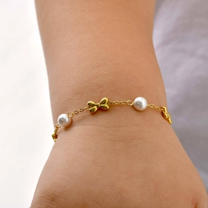Detailed close-up of girls' golden bow bracelet with pearls on wrist