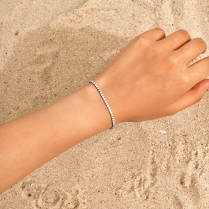 Makroaufnahme eines silbernen Tennisarmbands mit runden Zirkonia auf Strandhintergrund