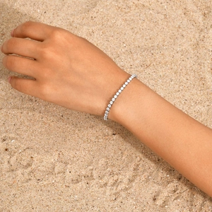 Tennisarmband aus Edelstahl mit Zirkonia-Steinen vor einem sandigen Strandhintergrund