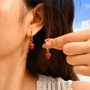 Chic gold hoop earrings with red strawberry enamel charms worn by a model outdoor