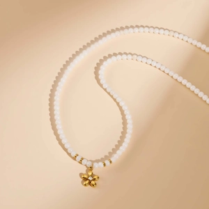 Vue détaillée du collier en perles blanches avec pendentif fleur dorée et cristal