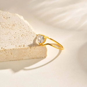 Détail d'une bague dorée ondulée avec un grand zircon poire sur un support en pierre