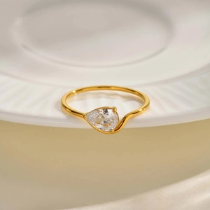 Bague vague dorée avec un zircon en forme de poire sur une plaque en céramique blanche