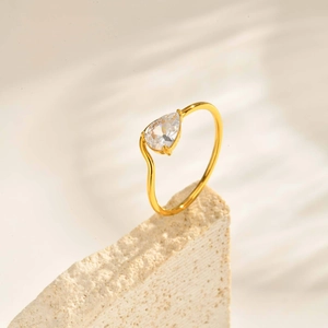 Détail du zircon poire sur un anneau doré ondulé avec fond en pierre naturelle