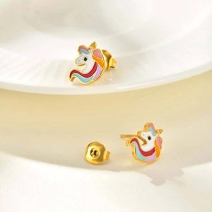 Detalle macro de pendientes de unicornio dorados con esmalte de colores en un plato blanco