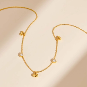 Elegant gold-plated cherry and heart zircon necklace on a soft beige background