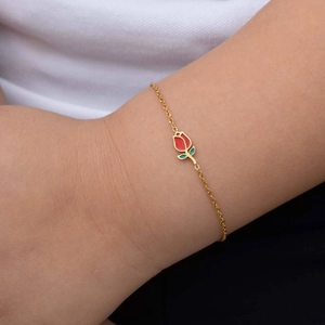 Detail of a minimalist gold bracelet with a red tulip enamel charm on a woman wrist