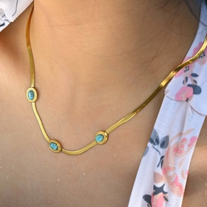 Dettaglio della collana a catena serpente dorata con pietre turchesi indossata da modella