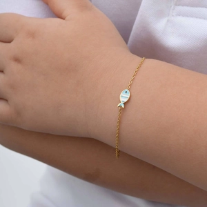 Close-up of a child wearing a gold chain bracelet with blue and white enamel fish pendant