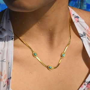 Collana a maglia serpente dorata con pietre turchesi su modella in una piscina estiva