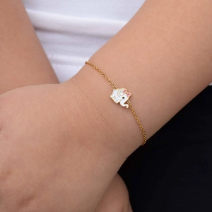 Detailed shot of a gold baby bracelet with a white elephant and pink bow charm