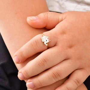 Detail of a child wearing a golden elephant ring with white enamel and pink bow