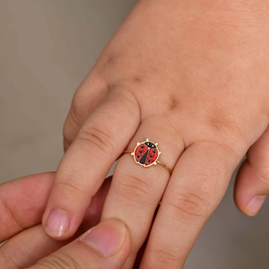 Close-up of a child wearing a cute red ladybug gold ring with enamel details
