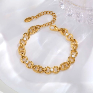 Detail of gold chain bracelet with pig nose links and white zircon stones on white fabric
