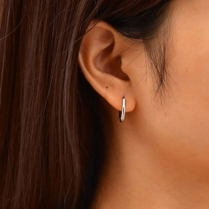 Close-up of minimalist silver U-shaped hoop earring on model showing sleek metal texture