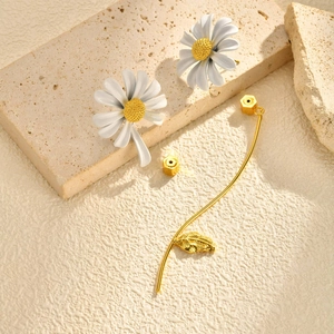 Détail de boucles d'oreilles marguerite avec tige dorée et pendentif feuille ciselée