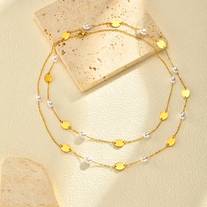Détail d'un collier multicouche en acier doré avec perles blanches et disques en métal