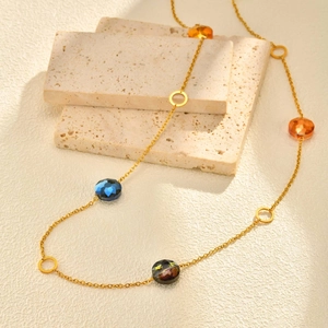 Long collier en acier inoxydable doré avec perles facettées sur socle en pierre minimaliste