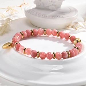 Détail d'un bracelet en perles de quartz rose avec breloque cœur doré sur céramique