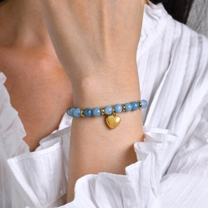 Gros plan d'un bracelet en perles bleu clair avec un pendentif coeur doré poli
